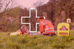 Emergency Medical Responders treating an unconscious patient in a field, with a large white medical icon in the background.
